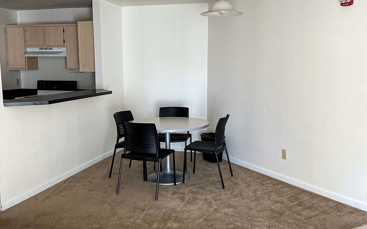 A table and four chairs sit in the corner of a room with a kitchen counter nearby.