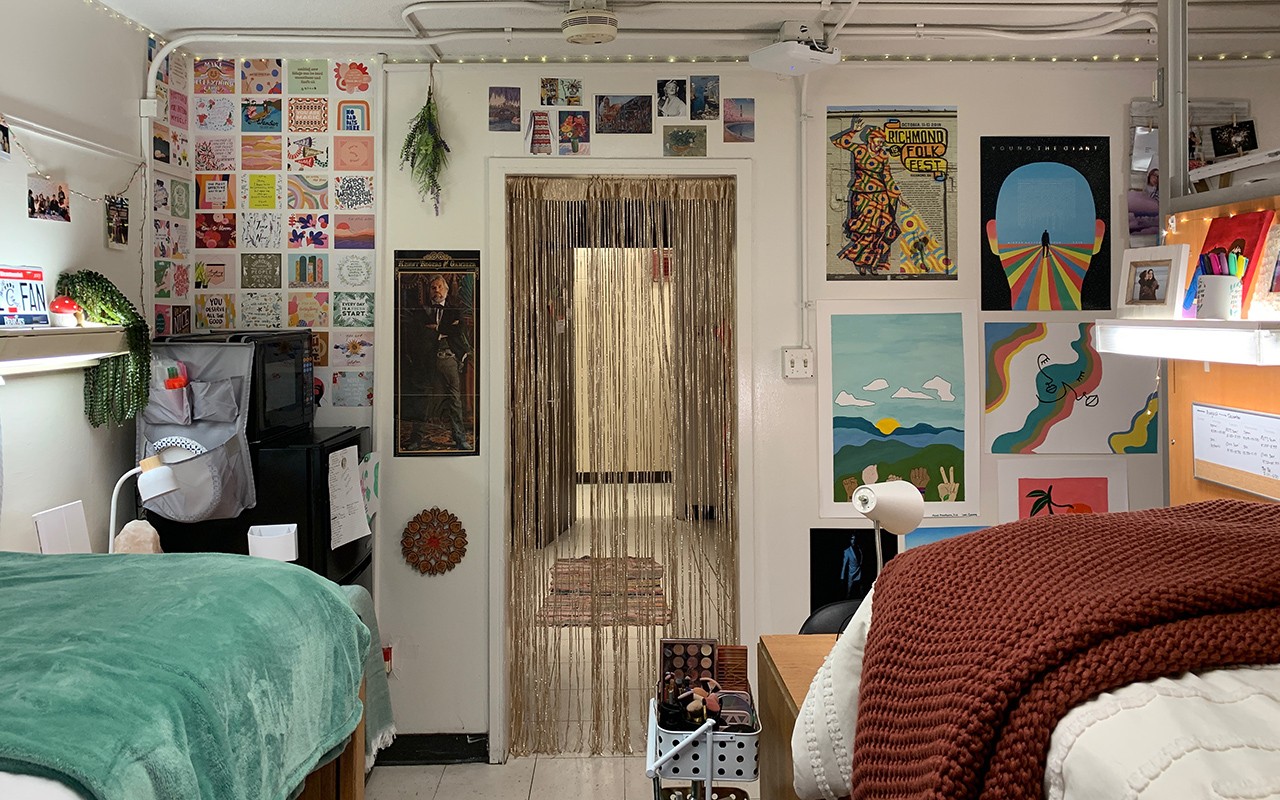 Residence hall double bedroom featuring many photos on the left wall by the hallway and art pieces to the right. A beaded curtain hangs in doorway