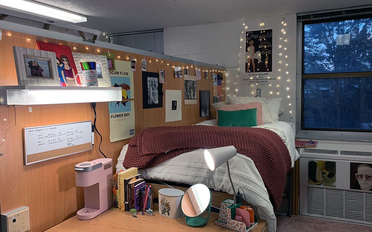 Residence hall room featuring partial wood wall next to bed decorated with art.