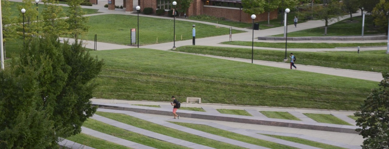 An elevated view of a campus green space with two students walking on pathways in the distance